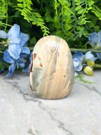 A natural stone, possibly a jade or slate, is displayed on a marble surface, surrounded by blue flowers.