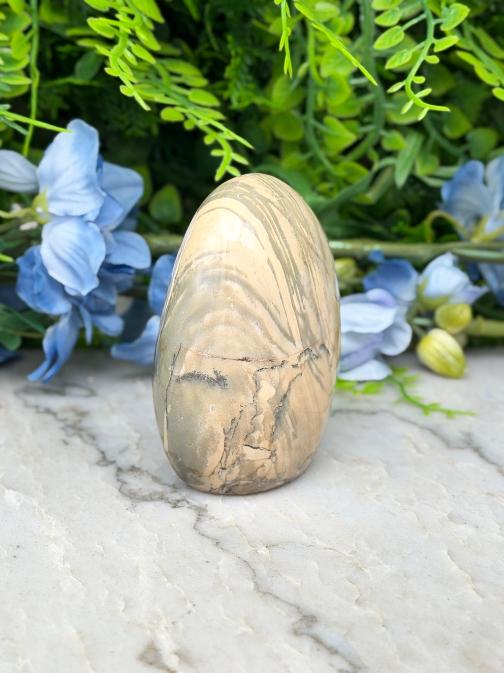 a stone with a unique, striped pattern, surrounded by a variety of blue flowers and green foliage.
