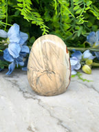 a natural stone, possibly a jade egg, placed on a marble surface surrounded by blue flowers.