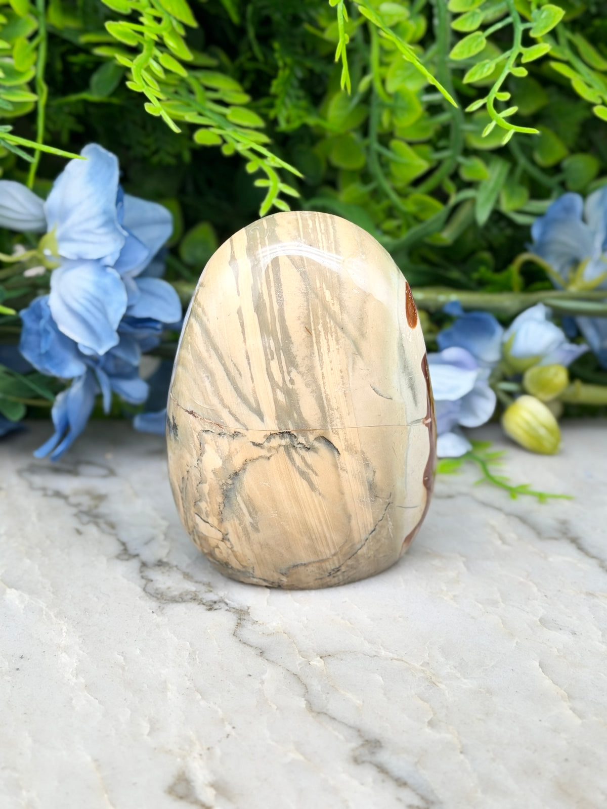 a natural stone, possibly a jade egg, placed on a marble surface surrounded by blue flowers.