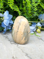 a natural stone, possibly a jade or slate rock, placed on a marble surface. The stone has a unique pattern and is surrounded by blue flowers, creating a visually appealing contrast.
