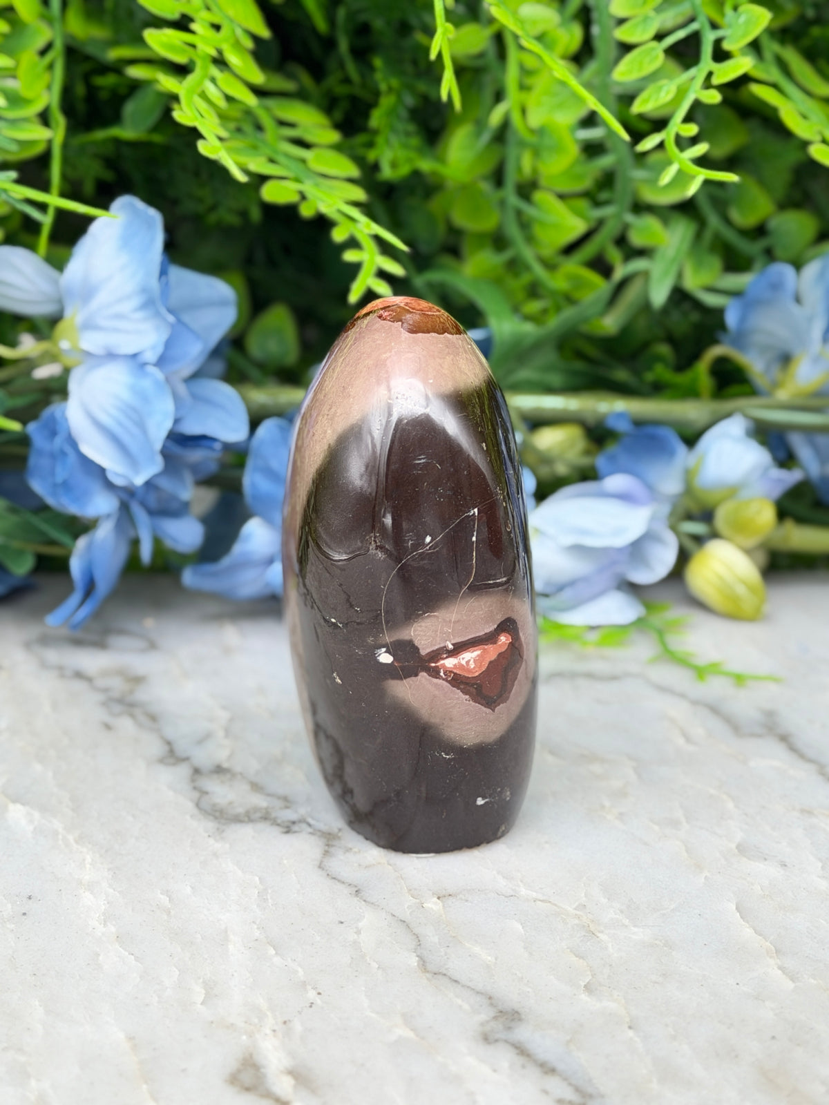 A brown, jagged-edged stone sits on a white marble surface, surrounded by blue flowers.