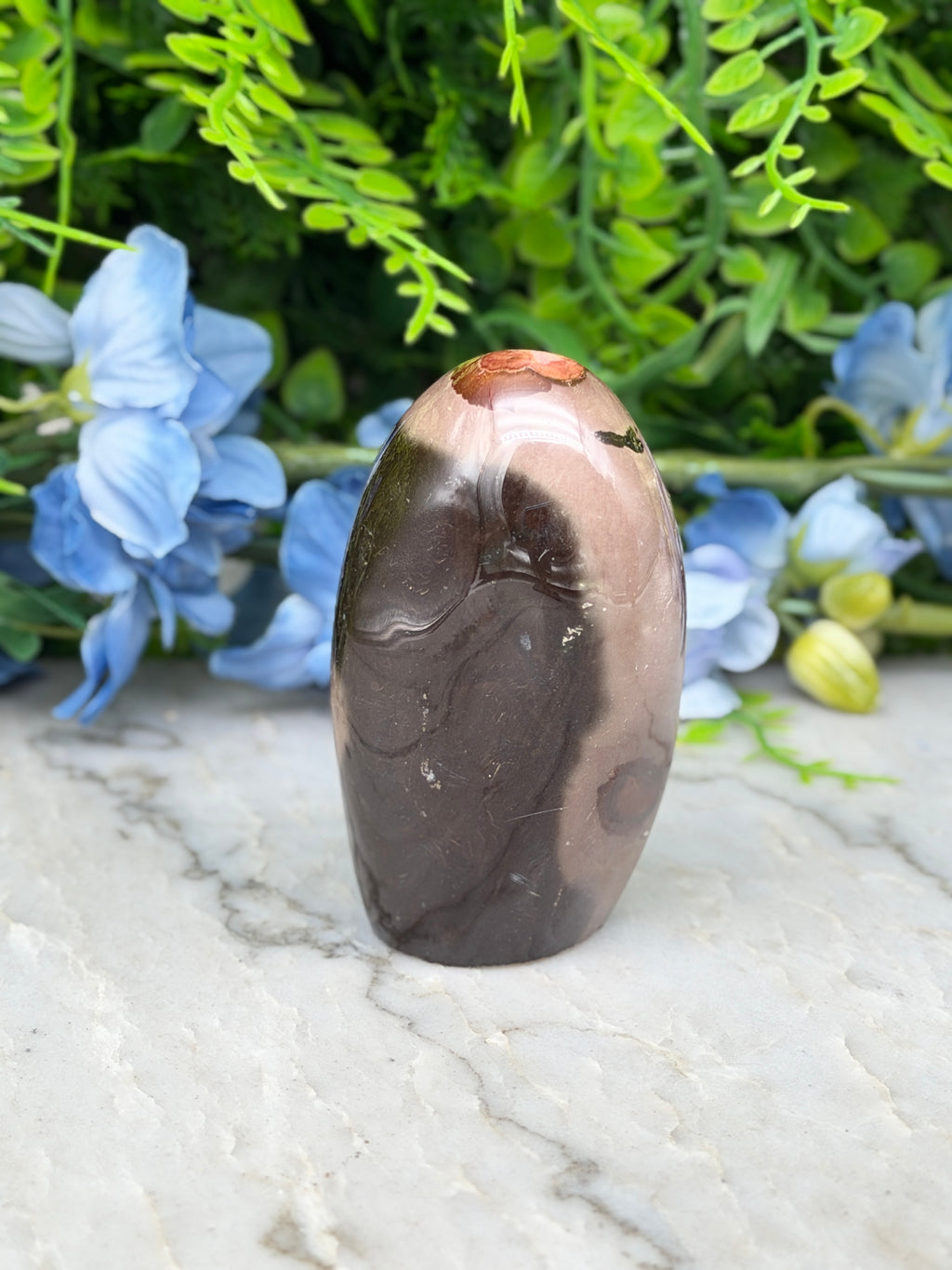 a brown and black stone vase placed on a marble surface, with a backdrop of blue flowers.