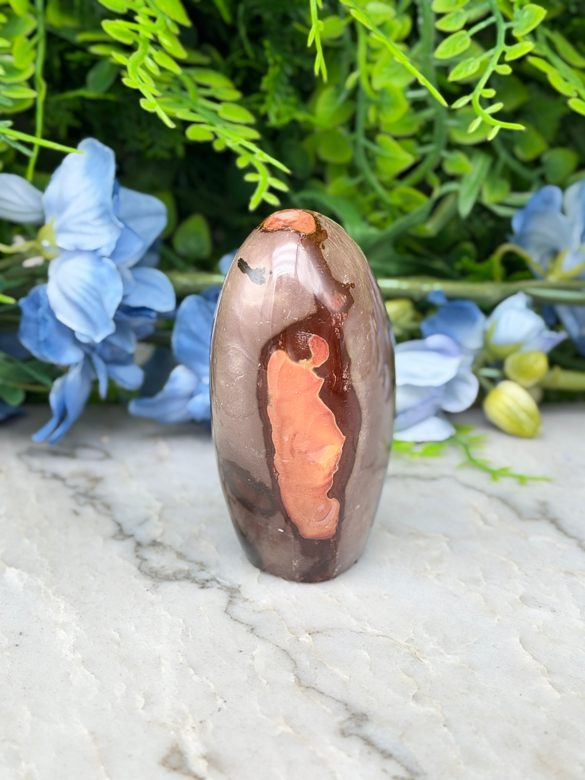 a brown and orange stone with a unique pattern, placed on a marble surface surrounded by blue flowers.