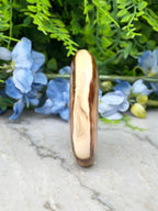 a tall, narrow, and brown-colored stone or gemstone, which appears to be a piece of amber or amberite, placed on a marble surface. The stone is surrounded by a variety of blue flowers, creating a visually appealing contrast between the natural and the artificial elements.