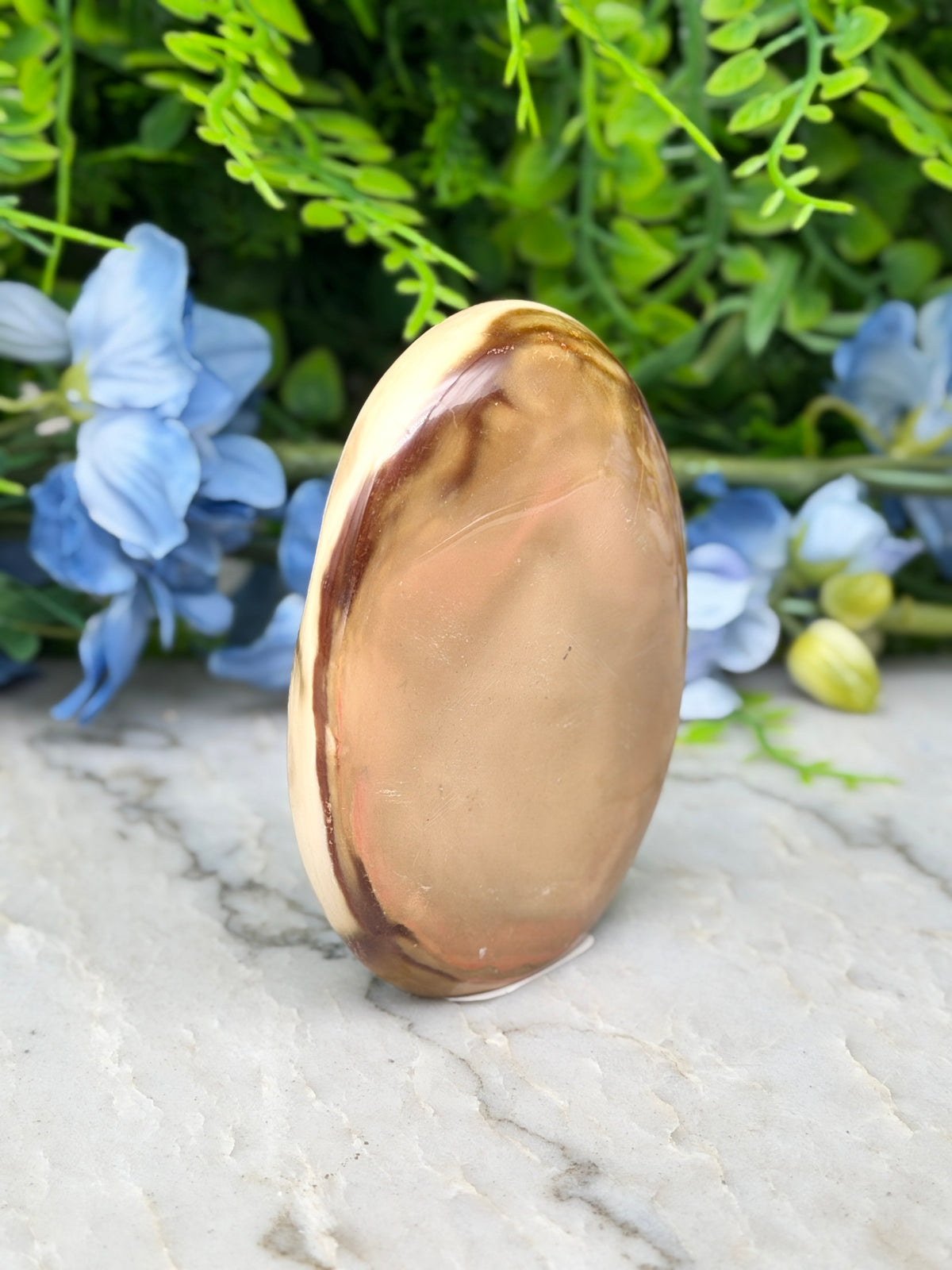 a brown oval-shaped stone or rock placed on a white marble surface, surrounded by blue flowers.