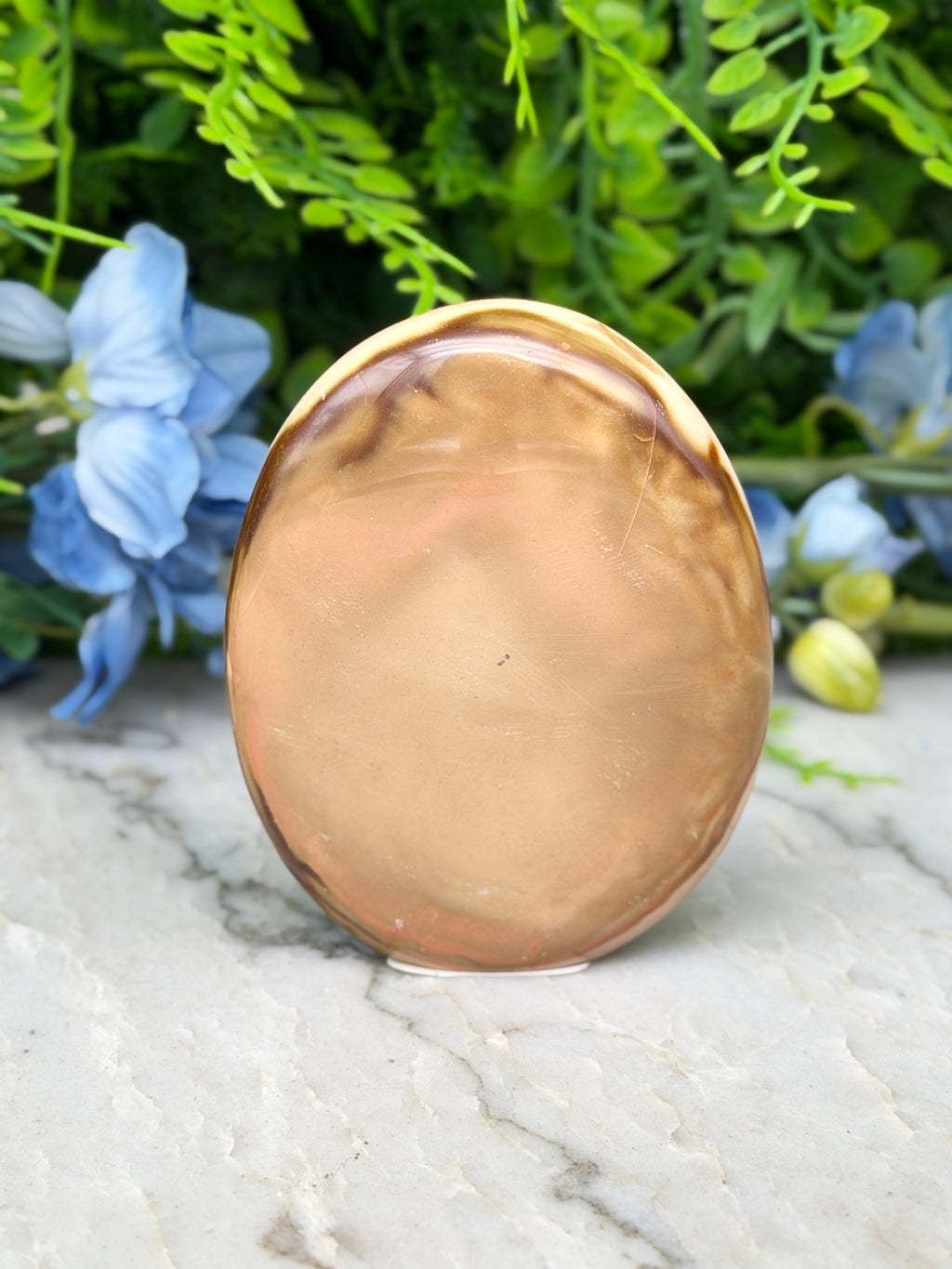 a round, brown stone or stone-like object placed on a marble surface, surrounded by blue flowers.