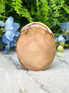 a round, brown stone or stone-like object placed on a marble surface, surrounded by blue flowers.