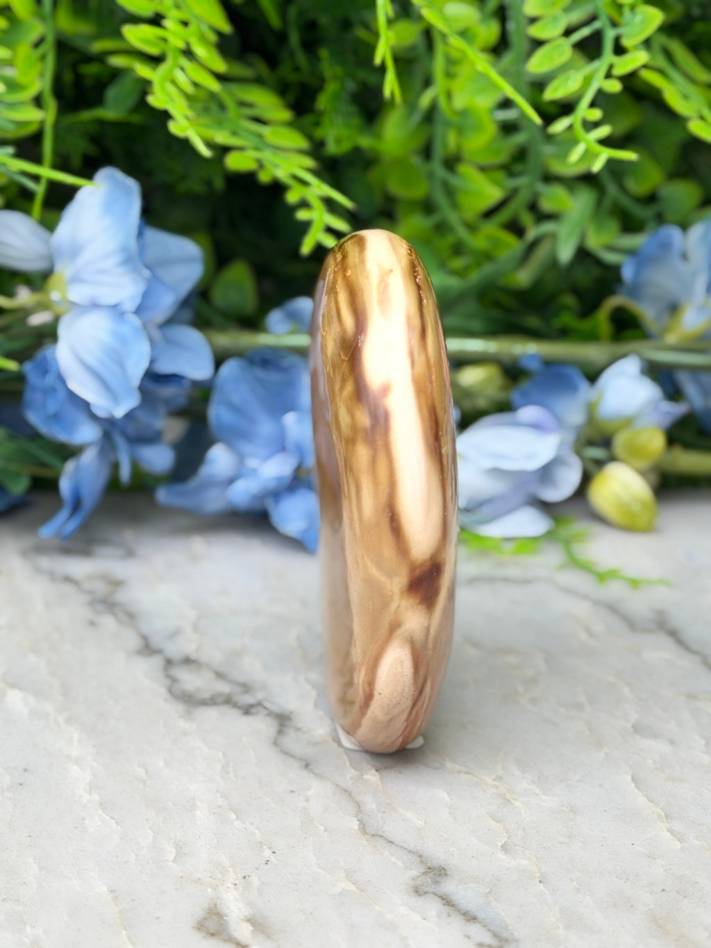 a brown, irregularly shaped stone or rock with a unique pattern, placed on a marble surface. The stone is surrounded by a variety of blue flowers, creating a visually appealing contrast.