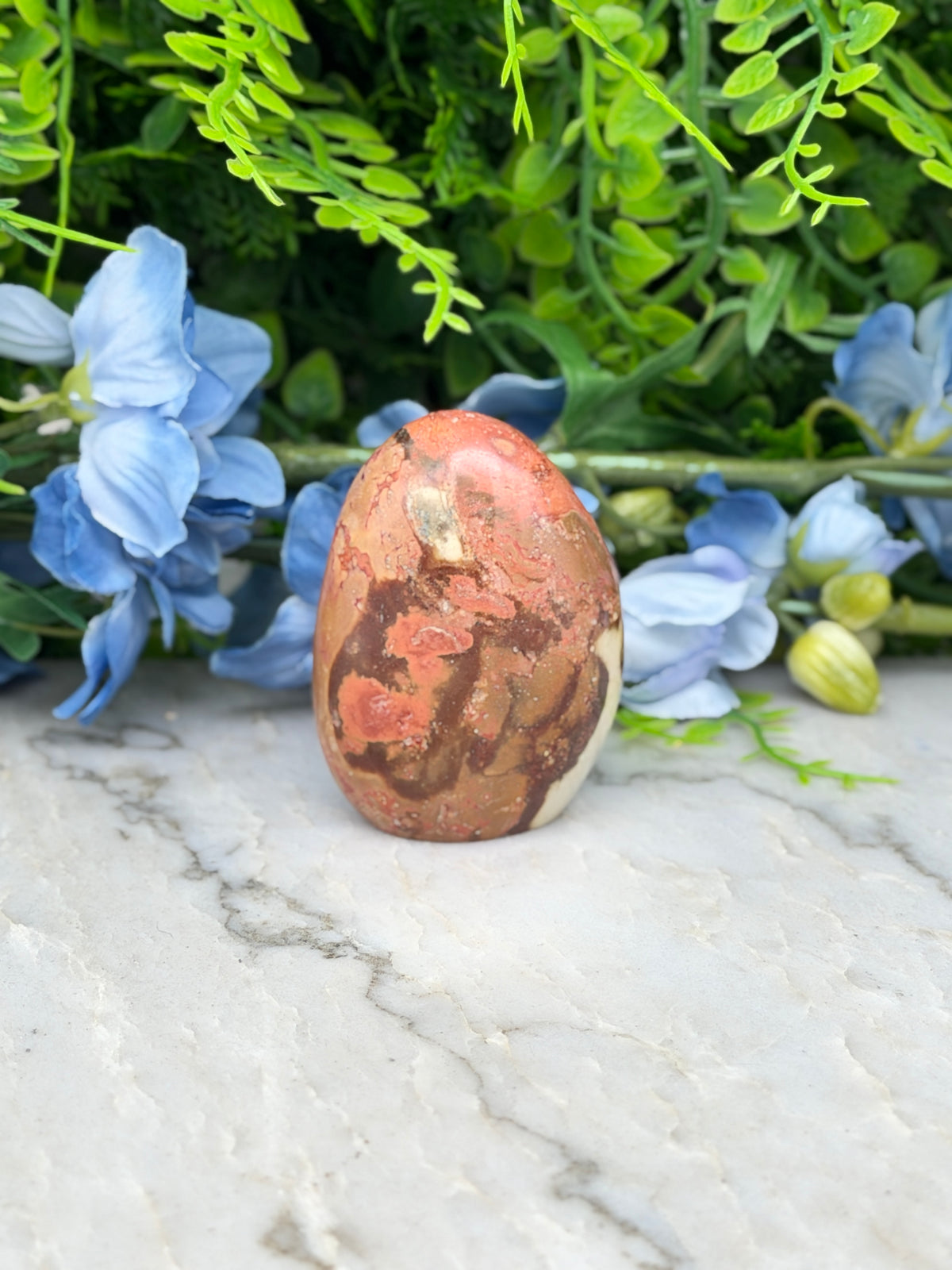 a brown and orange speckled rock sitting on a white marble surface, surrounded by blue flowers.