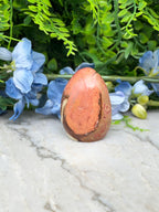 a brown and orange stone, possibly a jade egg, placed on a marble surface surrounded by blue flowers.