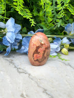 a red and brown stone, possibly a jade or amber, placed on a white marble surface. The stone is surrounded by blue flowers, creating a visually appealing contrast.