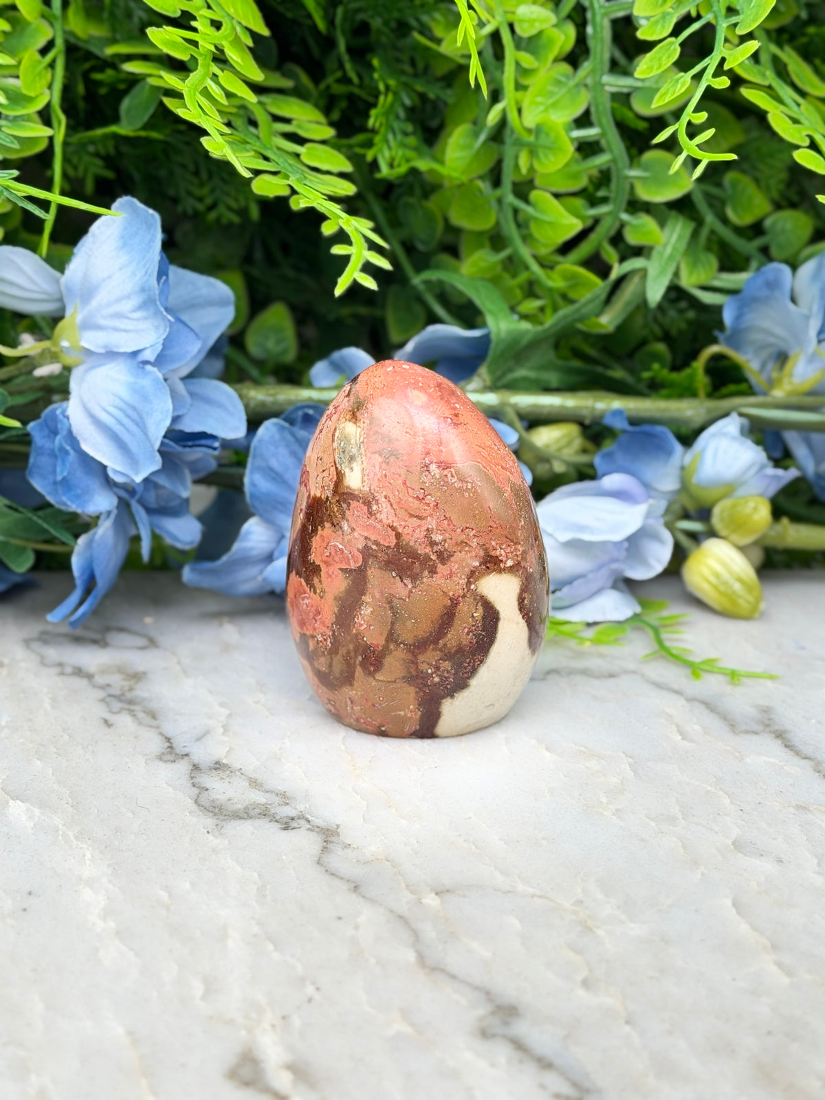 a brown and white speckled rock sitting on a marble surface, surrounded by blue flowers.