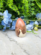 a single, unique object, a jade egg, placed on a marble surface. The jade egg has a brown and white color pattern and is surrounded by blue flowers.