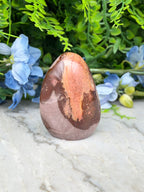 a brown and orange rock with a speckled surface, placed on a white marble surface. The rock is surrounded by blue flowers, creating a visually appealing contrast.
