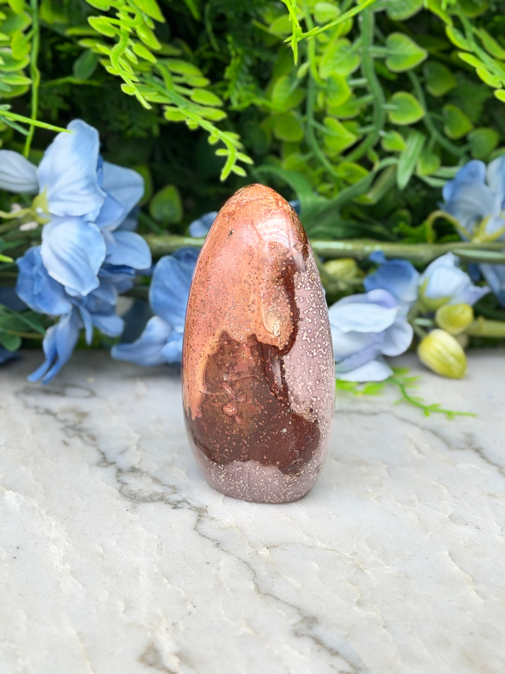 a brown, speckled rock sitting on a marble surface, surrounded by blue flowers.