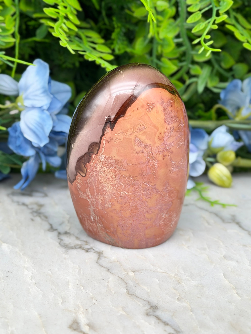 a brown, textured rock with a reflective surface, surrounded by blue flowers and greenery.