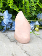 A pink crystal sits on a marble surface, surrounded by blue flowers and green foliage.