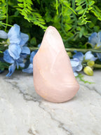 A pink crystal sits on a marble surface, surrounded by blue flowers and green foliage.