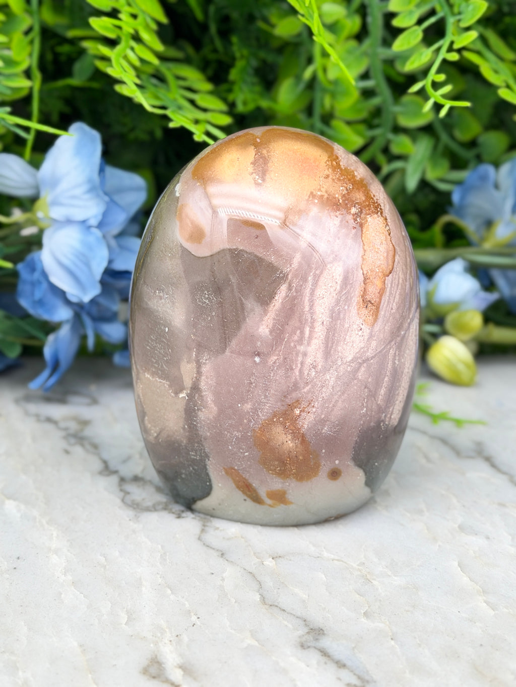 A jadeite, a type of jadeite gemstone, is displayed on a marble surface surrounded by blue flowers.