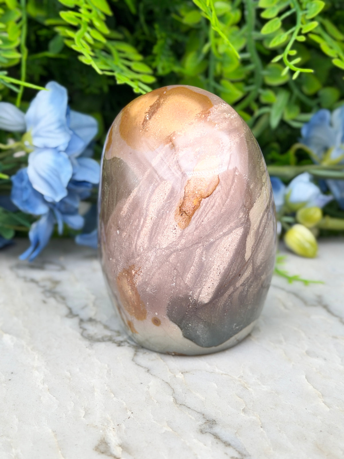 a large, colorful rock with a unique pattern, placed on a marble surface surrounded by blue flowers.