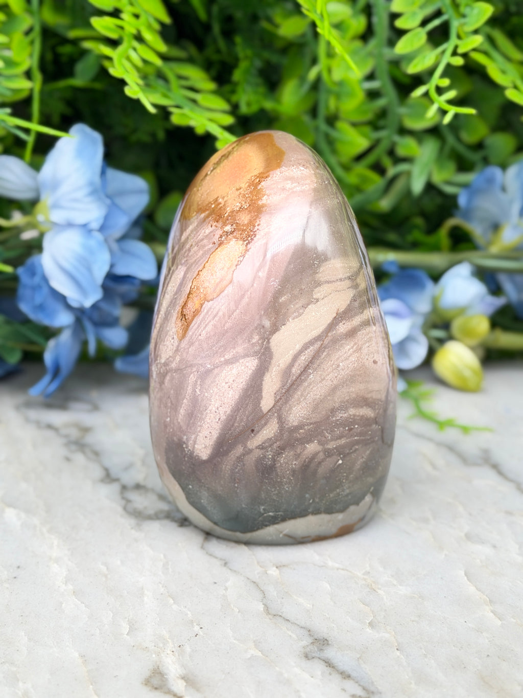 A jadeite, a type of natural stone, is displayed on a marble surface, surrounded by blue flowers.
