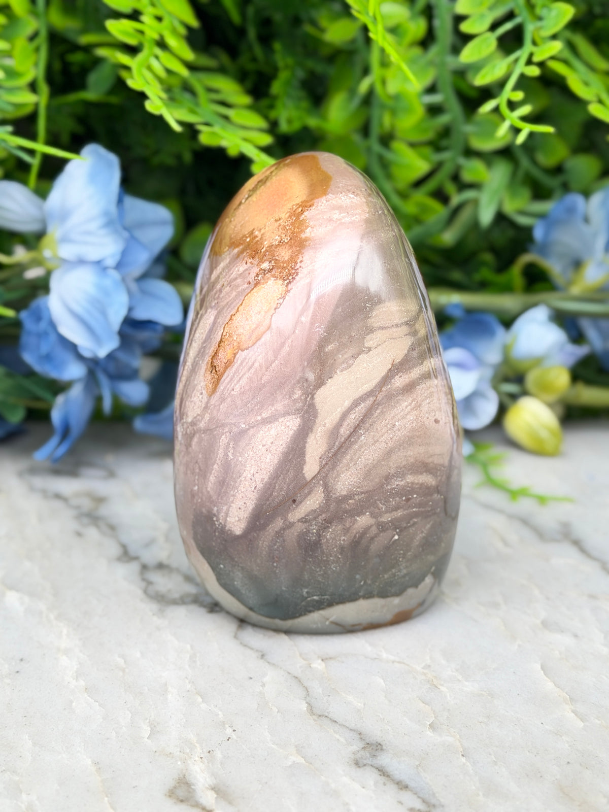 A jadeite, a type of natural stone, is displayed on a marble surface, surrounded by blue flowers.