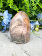 A jadeite, a type of jadeite gemstone, is displayed on a marble surface surrounded by blue flowers.