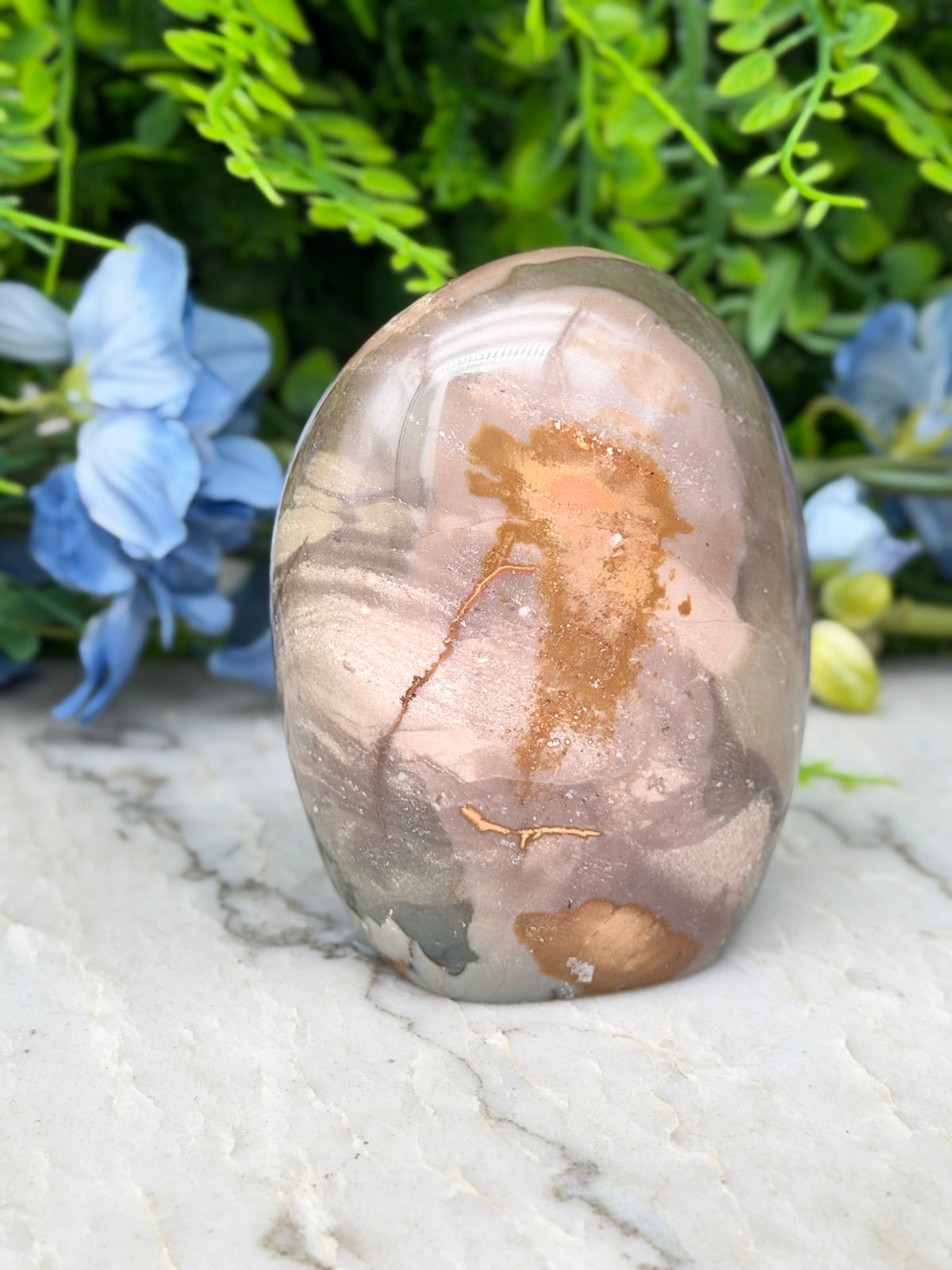 A jadeite, a type of agate, is displayed on a marble surface, surrounded by blue flowers.