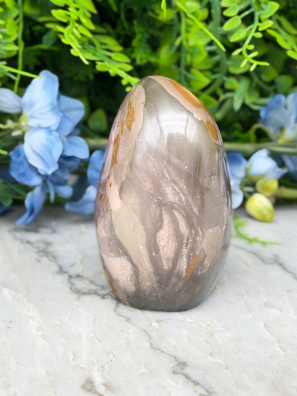 A jadeite, a type of jadeite gemstone, is displayed on a marble surface surrounded by blue flowers.