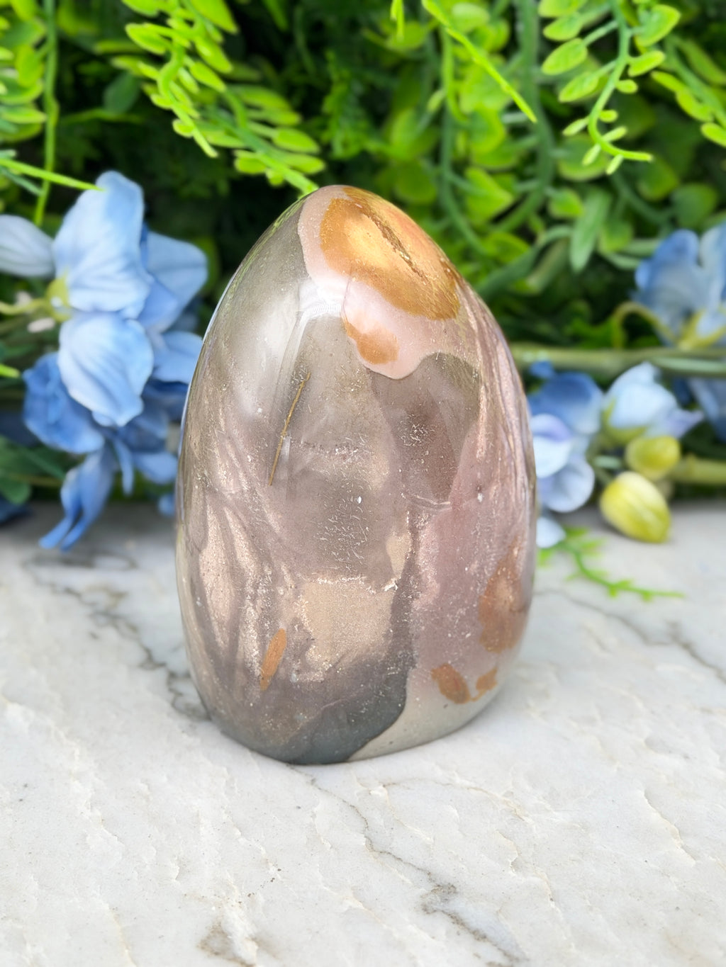 A jadeite, a type of agate, is displayed on a marble surface, surrounded by blue flowers.