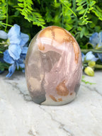 A jadeite, a type of jadeite gemstone, is displayed on a marble surface surrounded by blue flowers.