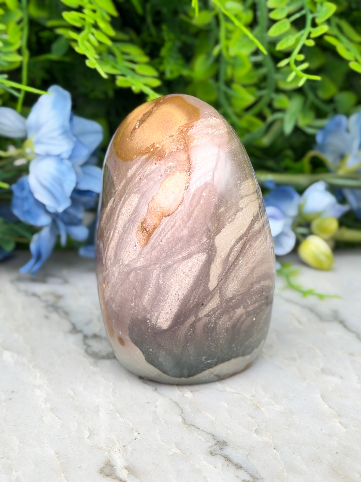 A jadeite, a type of natural stone, is displayed on a marble surface, surrounded by blue flowers.
