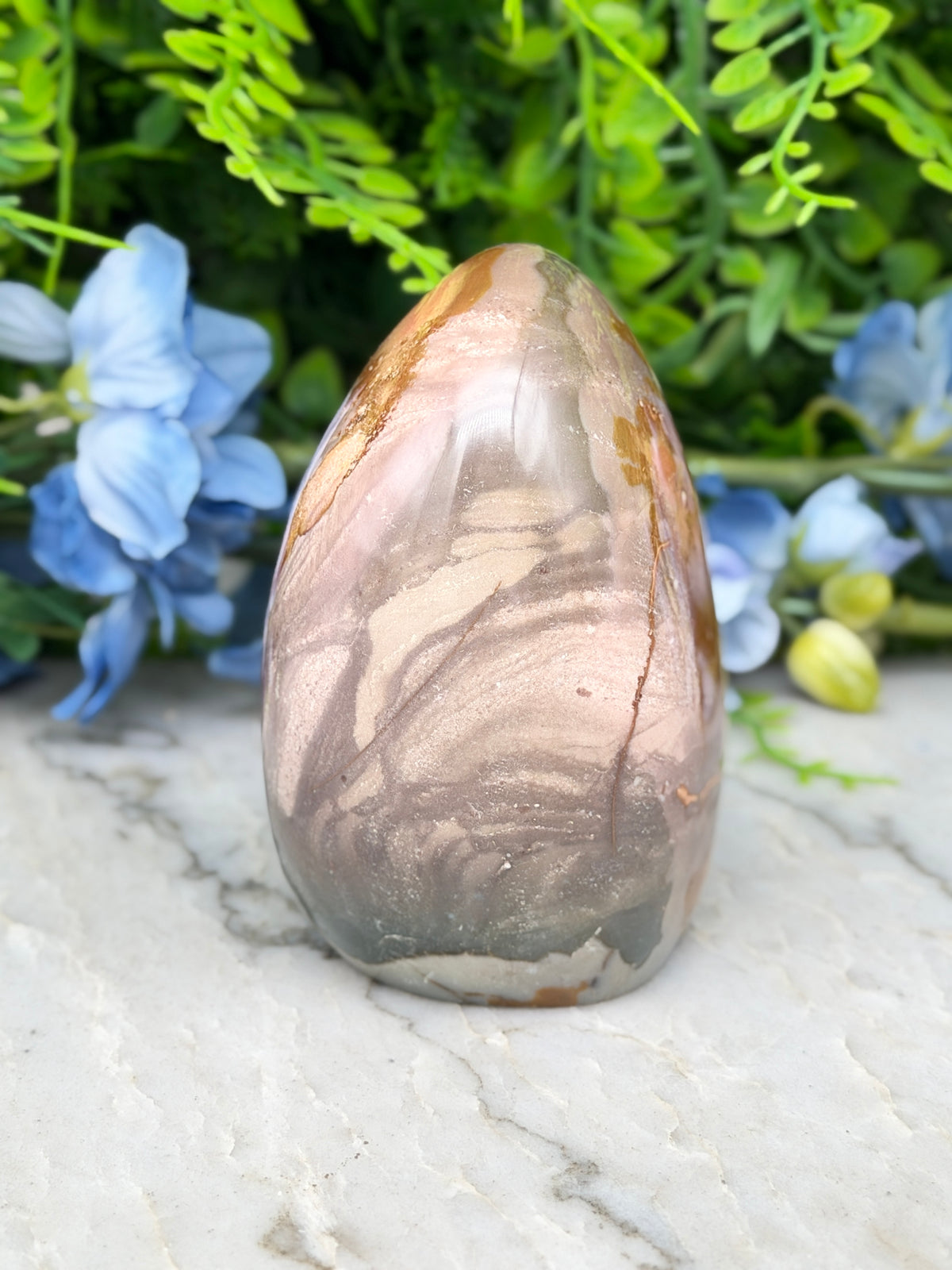 A jadeite, a type of natural stone, is displayed on a marble surface surrounded by blue flowers.