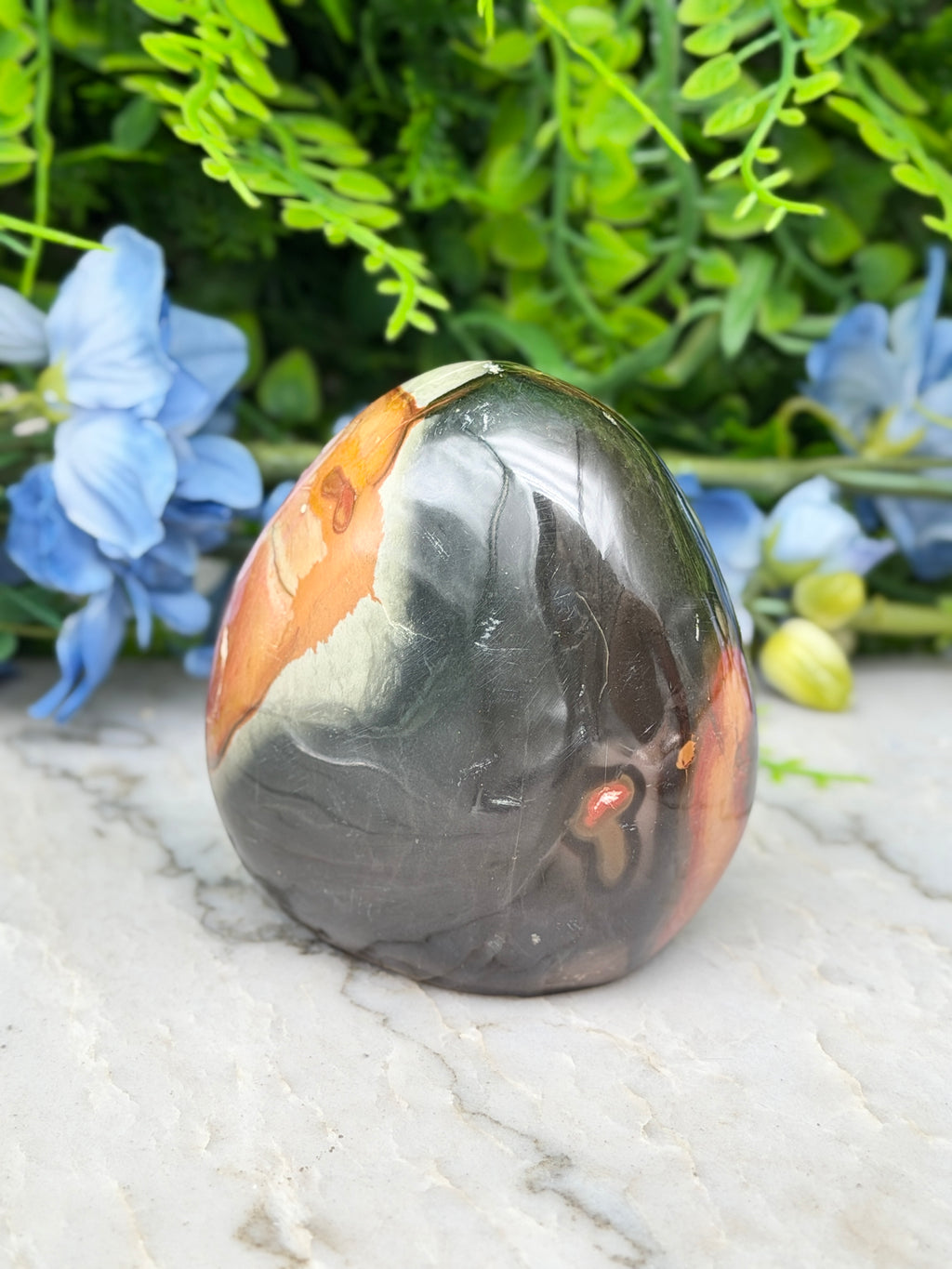 A jadeite, a type of jadeite gemstone, is displayed on a marble surface, surrounded by blue flowers.