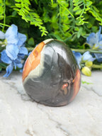 A jadeite, a type of jadeite gemstone, is displayed on a marble surface, surrounded by blue flowers.