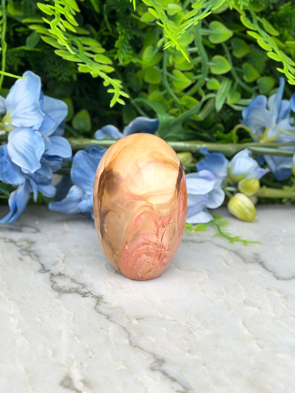 a marble-like stone or rock with a unique, swirling pattern, surrounded by blue flowers and green foliage.