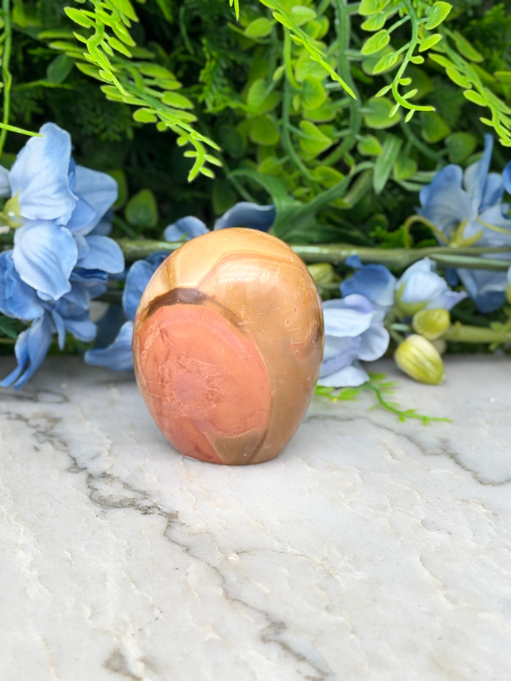 a stone or rock with a unique, textured surface, surrounded by a variety of green plants and blue flowers.