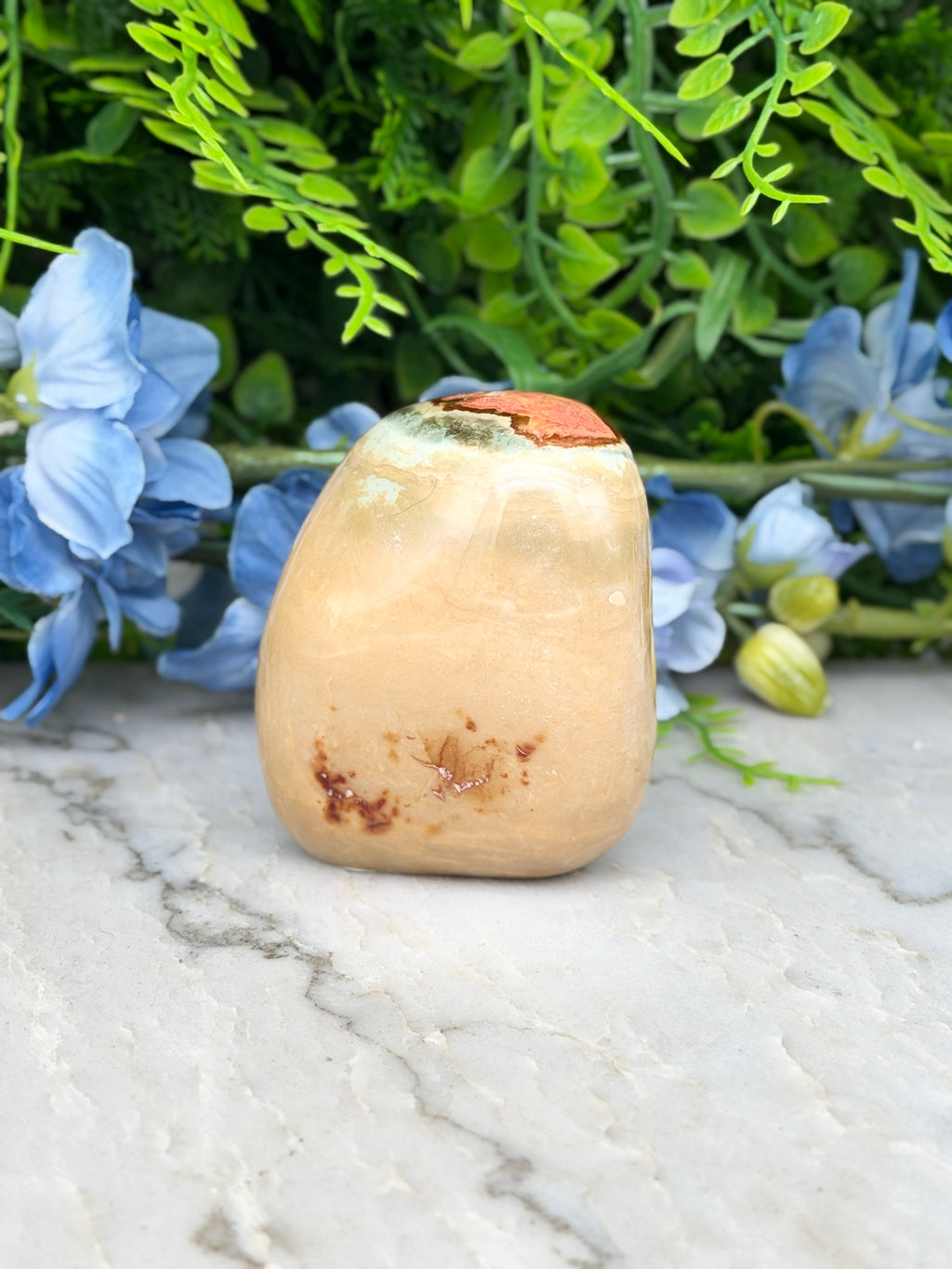 a light brown stone with a reddish-brown top, placed on a marble surface surrounded by blue flowers.