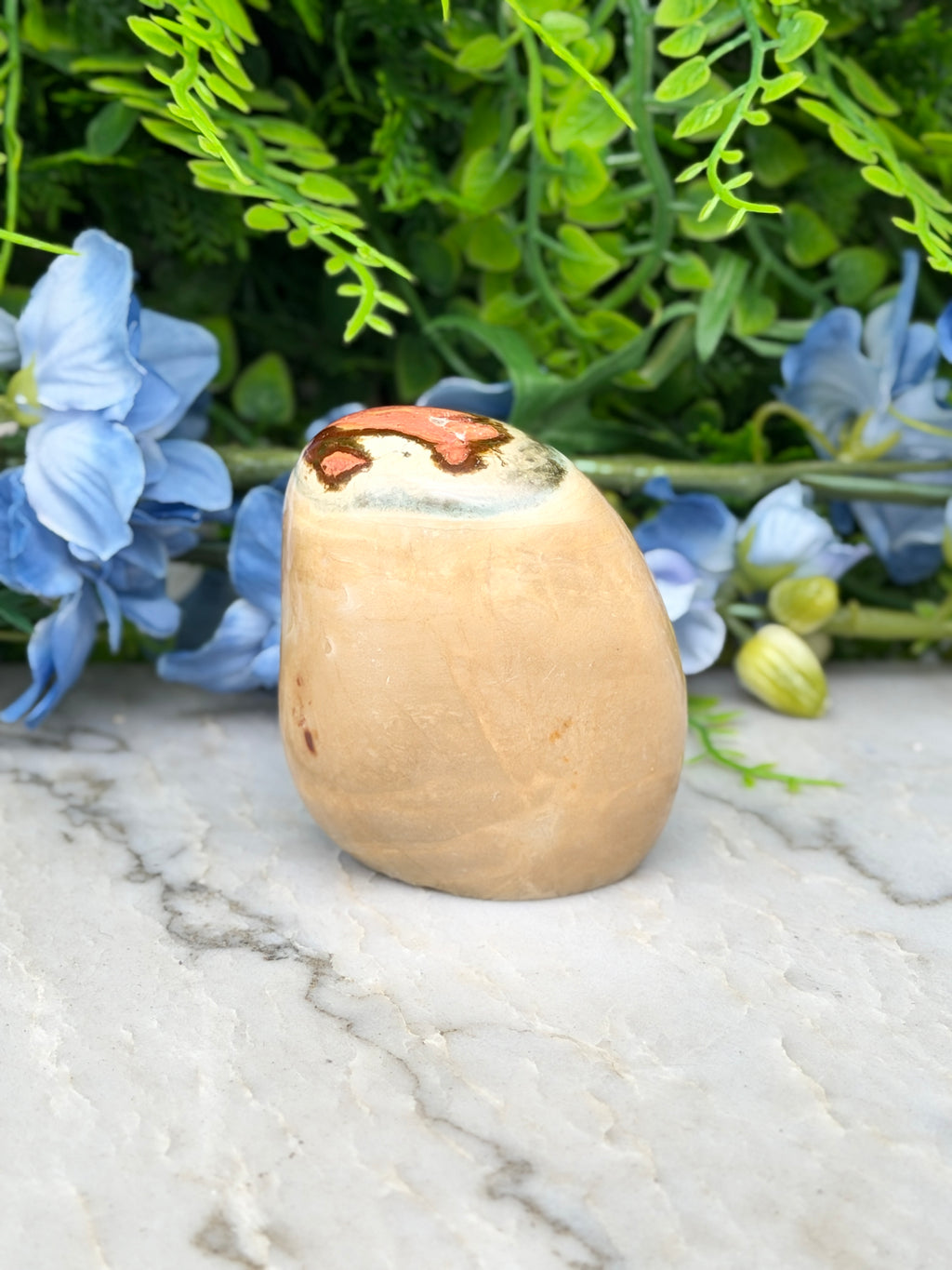 a light brown, oval-shaped object with a red and brown pattern on its surface, placed on a marble surface surrounded by blue flowers.