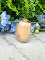 a light brown stone with a red spot on it, placed on a marble surface surrounded by blue flowers.