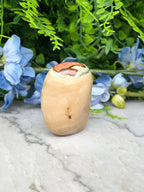 a light brown stone with a red and orange pattern on top, placed on a marble surface surrounded by blue flowers.