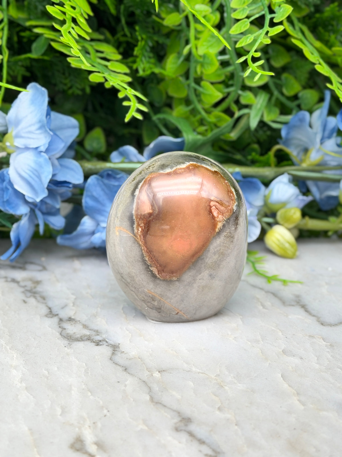 a stone with a unique, irregular shape, surrounded by a variety of blue flowers and green foliage.