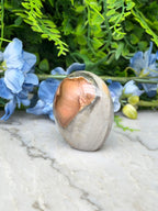 a large, oval-shaped rock with a copper-colored interior, placed on a marble surface. The rock is surrounded by blue flowers, creating a visually appealing contrast between the natural and man-made elements.