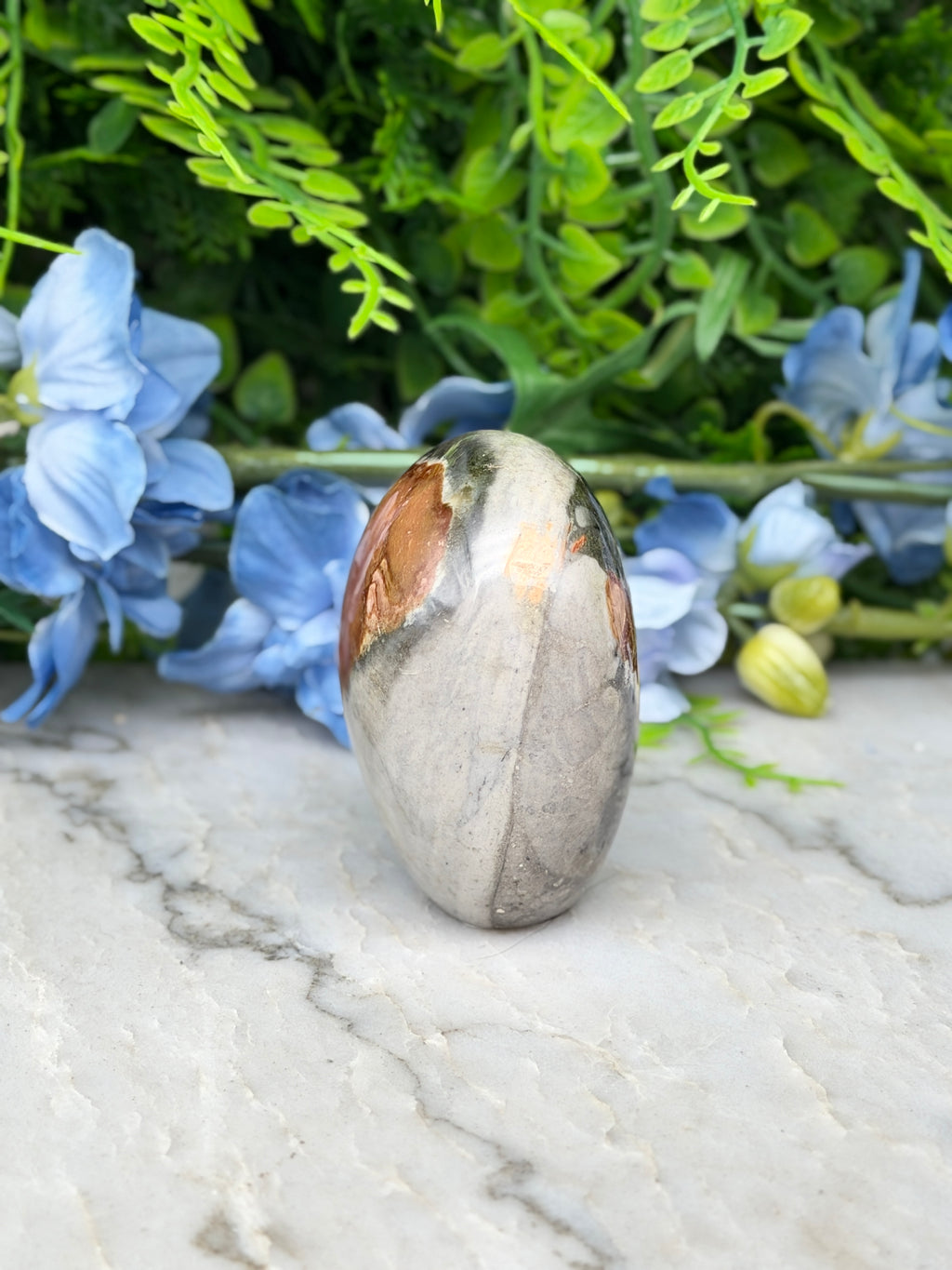 a stone with a unique pattern, surrounded by blue flowers and green foliage.