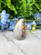 a large, oval-shaped stone with a mix of brown and gray hues, placed on a marble surface. The stone is surrounded by a variety of blue flowers, creating a visually appealing contrast.