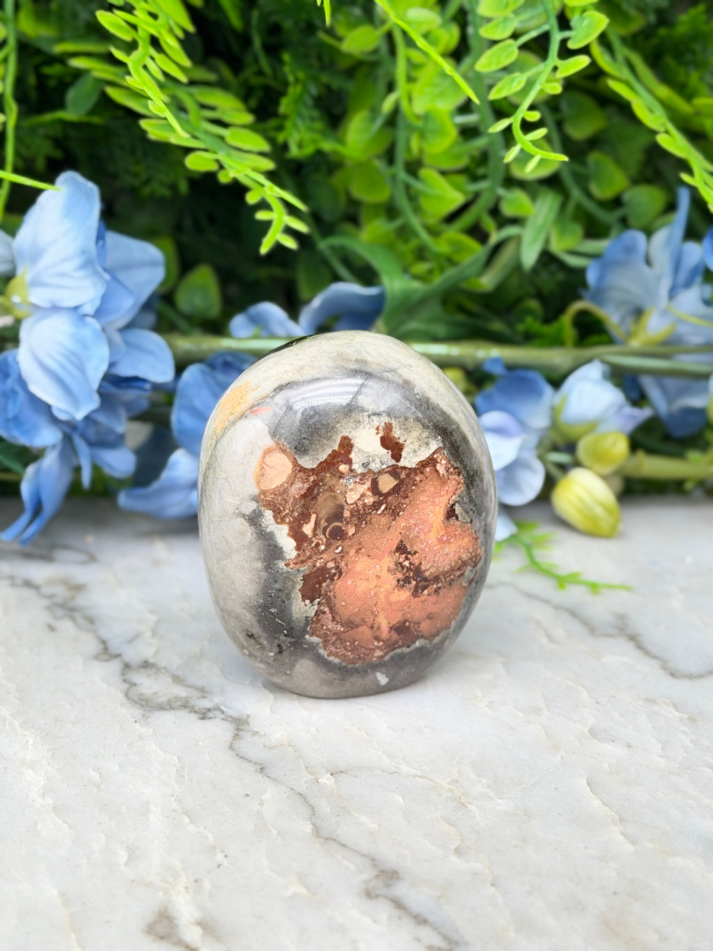 a close-up of a jadeite gemstone, which is a type of jadeite, set against a backdrop of lush green foliage and blue flowers.