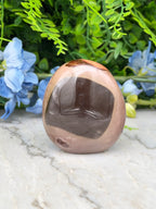 A brown and black stone sits on a marble surface, surrounded by blue flowers and green foliage.