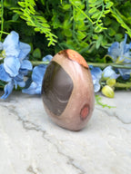 a brown and orange stone with a black and brown pattern, placed on a white marble surface. The stone is surrounded by blue flowers, creating a visually appealing contrast.