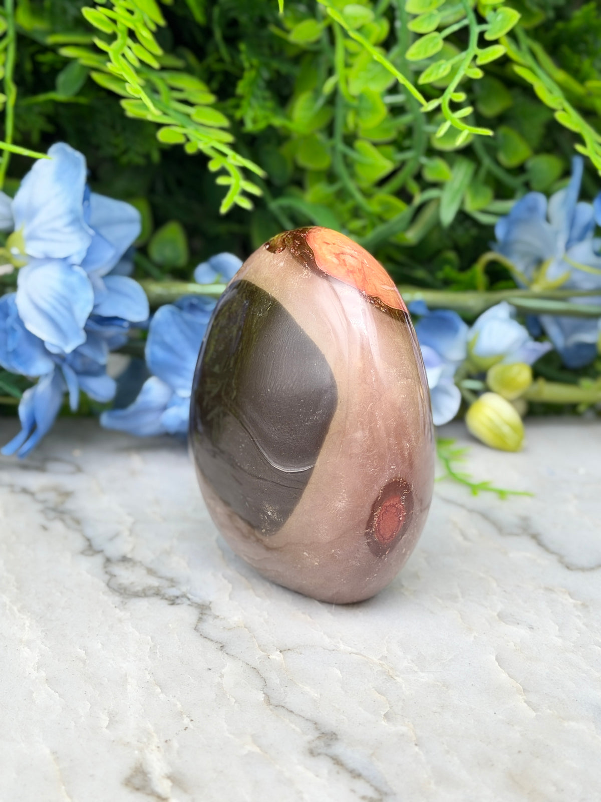 a brown and orange stone with a black and brown pattern, placed on a white marble surface. The stone is surrounded by blue flowers, creating a visually appealing contrast.